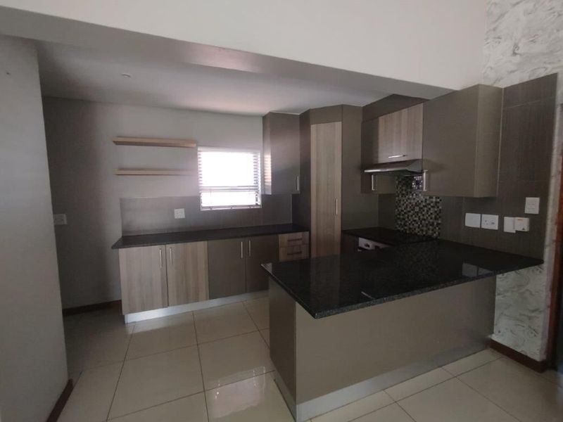 Modern kitchen featuring dark granite countertops, ample built-in cabinetry, a mosaic tile backsplash, and neutral tiled flooring in an open-plan layout.