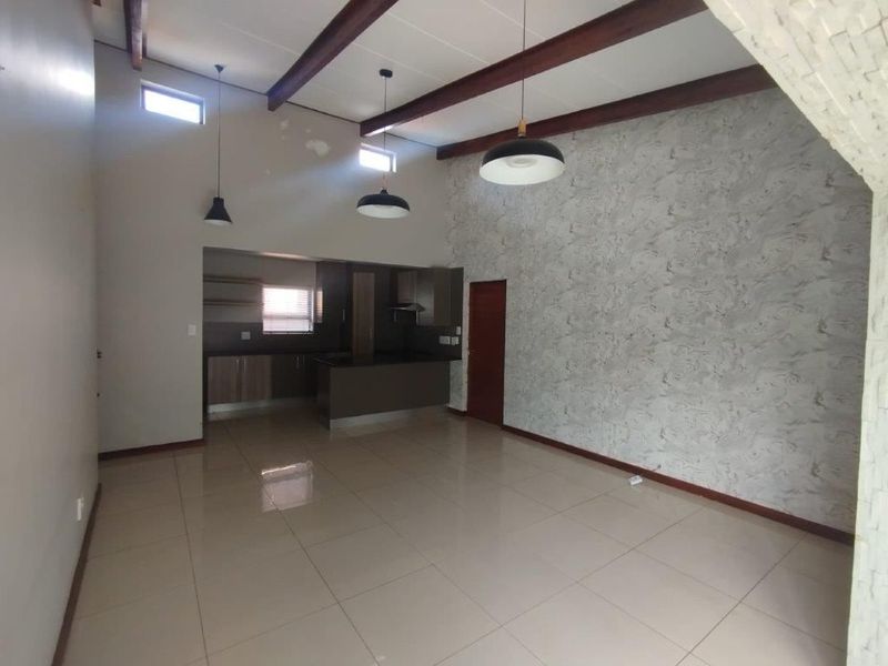Spacious open-plan living and kitchen area featuring high ceilings with exposed timber beams, tiled flooring, and a modern textured feature wall.