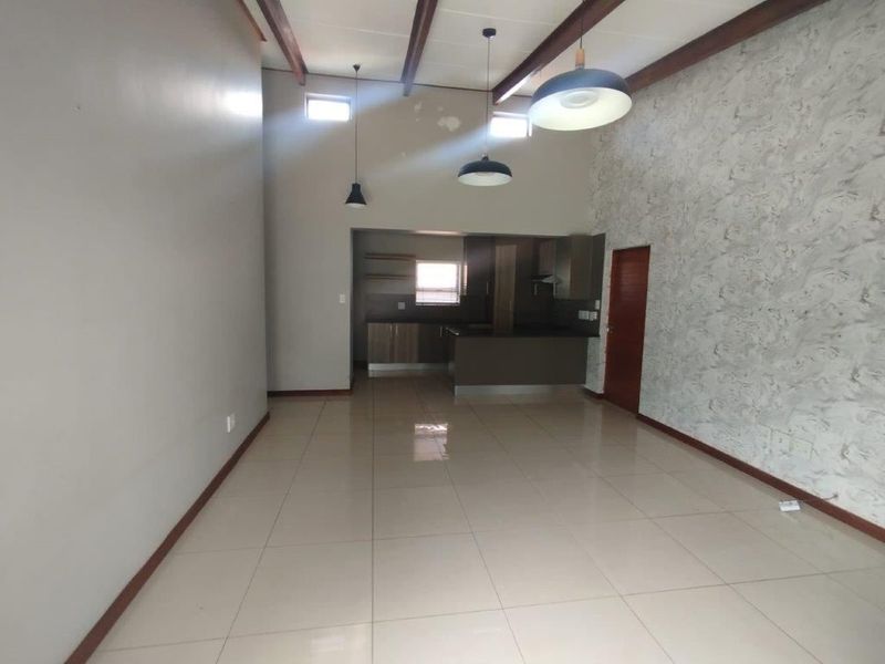 Spacious open-plan living area featuring tiled floors, exposed timber beams, and a kitchen with built-in cabinetry and island, offering a versatile layout.