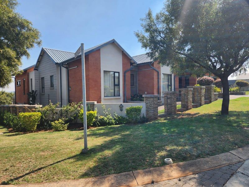 A well-maintained residential property featuring a brick and metal facade, stone-clad pillars, and established garden landscaping viewed from the street.