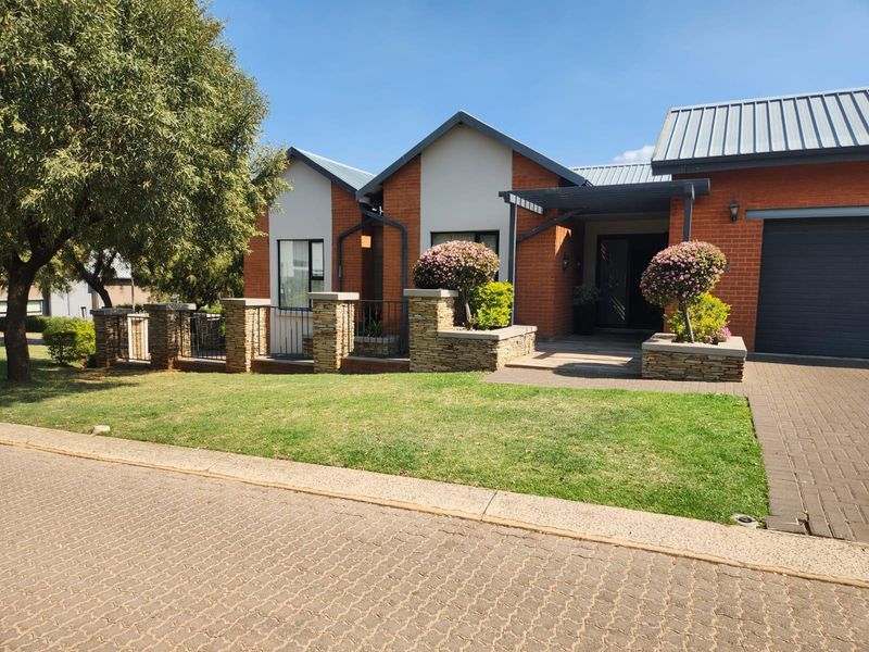 A well-maintained single-story brick house featuring a paved driveway, stone-clad garden walls, and a covered entrance with a modern metal roof.