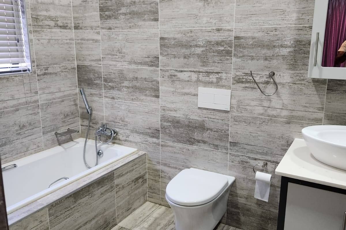 Modern bathroom featuring full-height wood-look wall tiling, a built-in bathtub with handheld shower, wall-mounted toilet, and a vanity with a vessel sink.