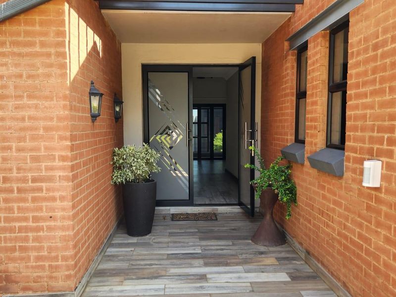 Inviting entrance featuring exposed brick walls, a modern pergola, and stylish wood-look tiled flooring leading to a glass-panelled front door.