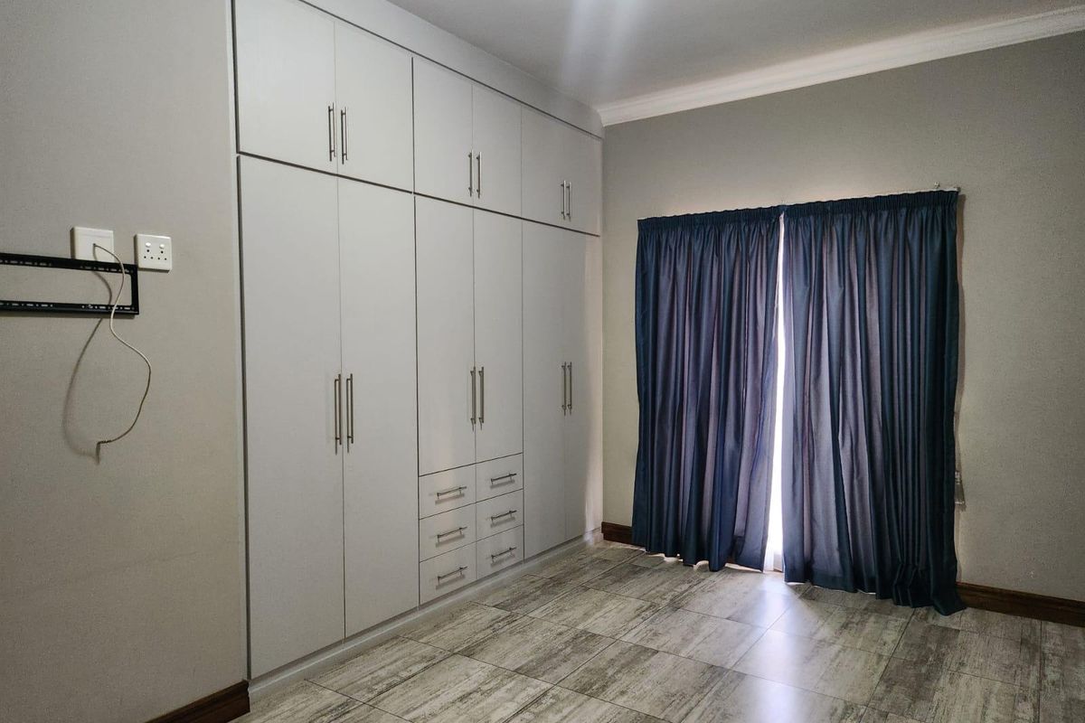 A clean, empty bedroom featuring modern light-grey built-in cupboards, wood-look tiled flooring, and neutral wall finishes.