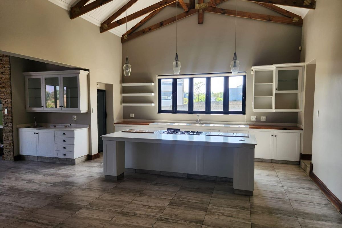 Spacious modern kitchen featuring a large central island, gas hob, vaulted ceilings with exposed timber trusses, and ample built-in cabinetry.