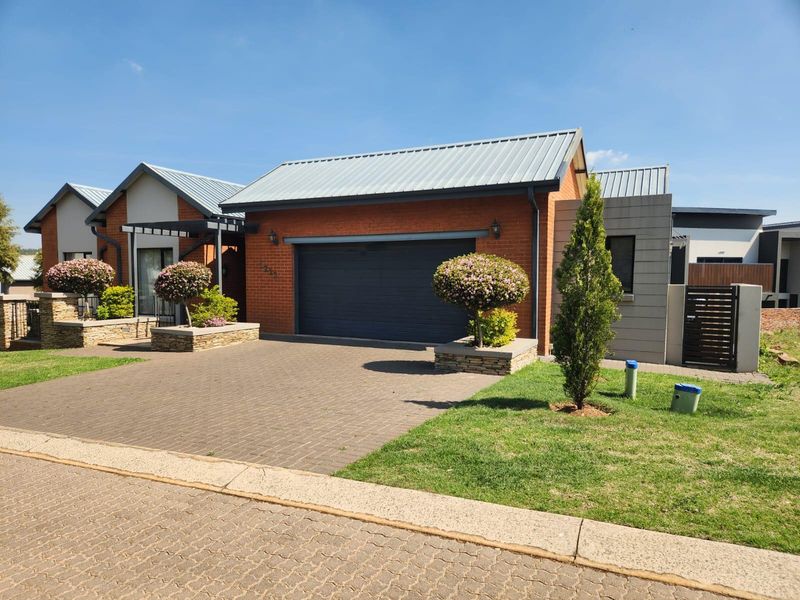 A well-maintained modern house exterior featuring a brick facade, metal roofing, a paved driveway, and a double garage with integrated stone-clad planters.