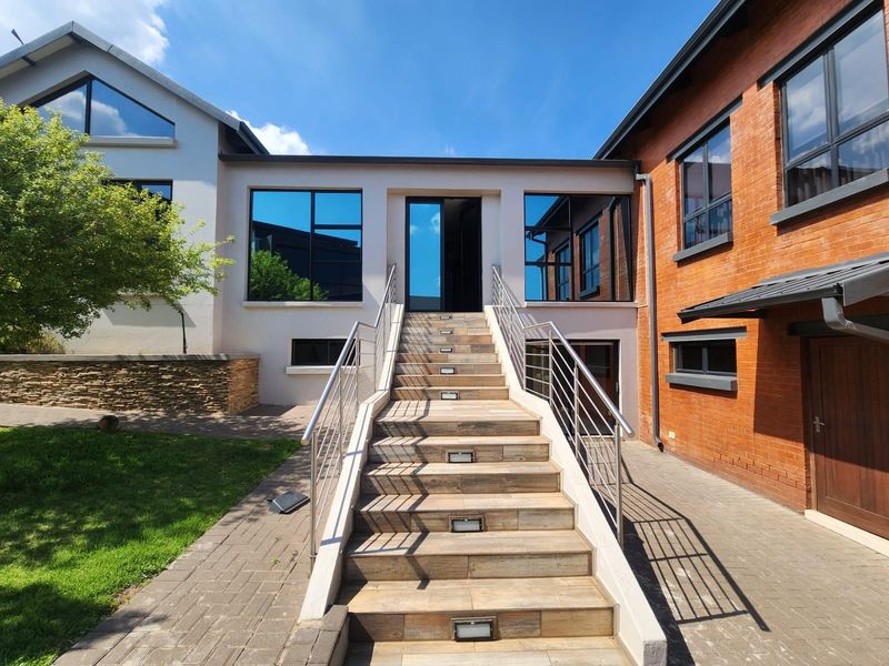 A well-maintained rear exterior featuring a modern tiled staircase with stainless steel railings, recessed lighting, and a combination of brick and plastered finishes.