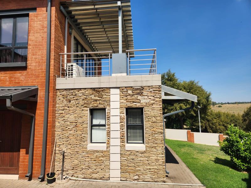 Rear elevation of a modern house featuring stone cladding, a brick facade, and an upper-level balcony with a stainless steel balustrade.