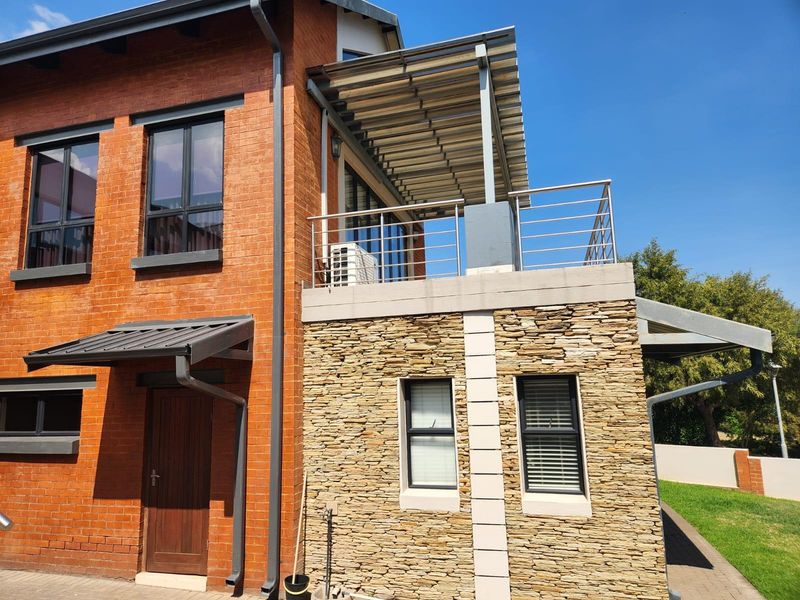 Rear view of a double-storey house featuring a combination of exposed brick and stone cladding, with an upper-level balcony and metal awning.