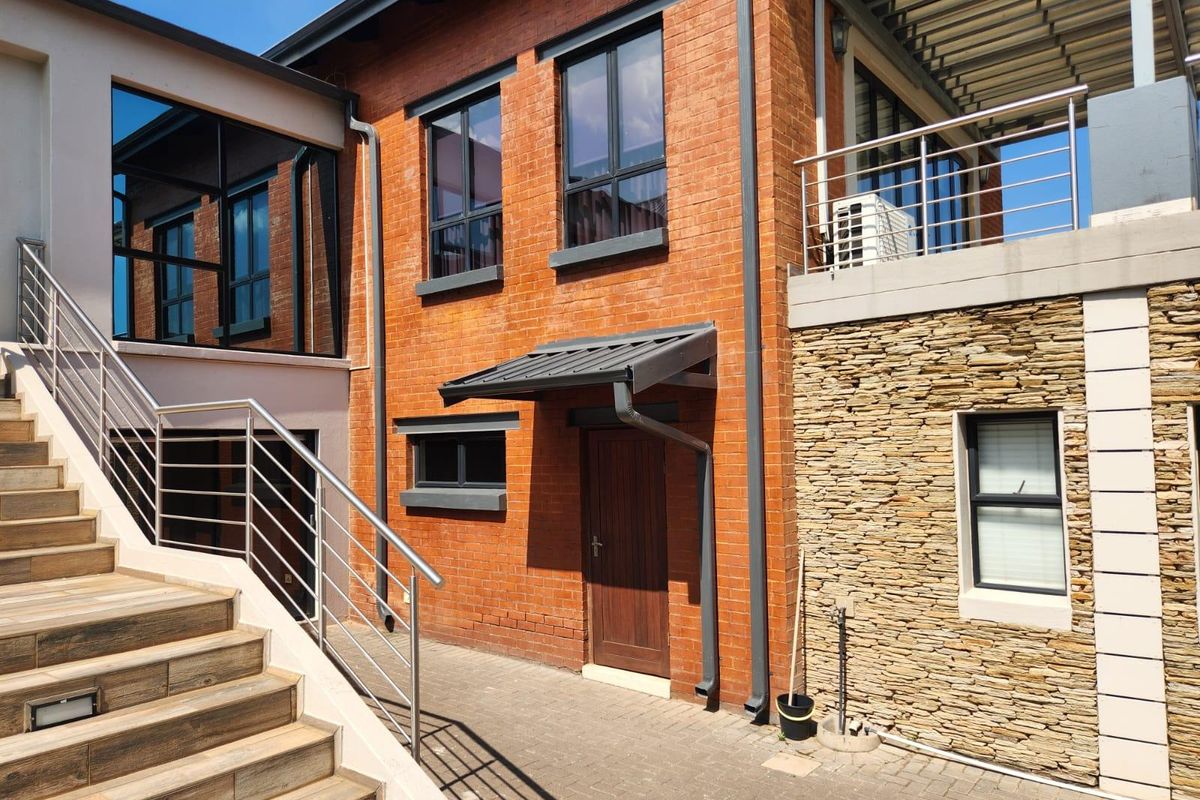 Rear exterior view featuring a combination of exposed brick and stone cladding, with a paved courtyard, external staircase, and modern stainless steel balustrades.