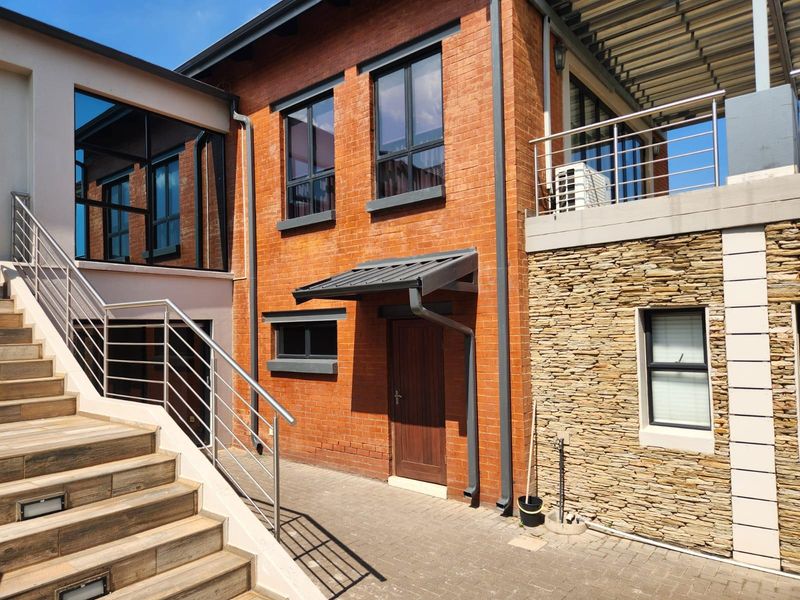 Rear exterior view featuring a combination of exposed brick and stone cladding, with a paved courtyard, external staircase, and modern stainless steel balustrades.