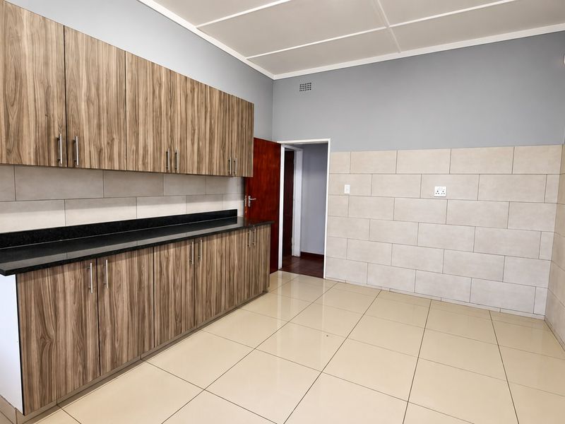 A clean, empty kitchen featuring modern wood-look cabinetry, dark granite countertops, neutral wall tiling, and light-colored floor tiles.