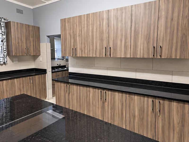 Modern kitchen featuring wood-grain cabinetry, black granite countertops, and a central island, providing ample workspace and storage.