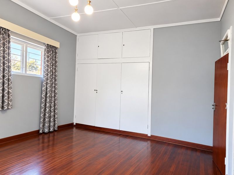A clean, empty bedroom featuring polished timber flooring, neutral grey walls, and extensive built-in cupboard storage with overhead cabinets.