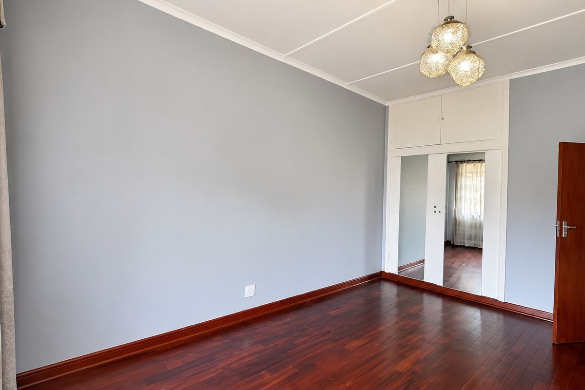 A bright, empty bedroom featuring polished hardwood flooring, built-in mirrored wardrobes with overhead storage, and neutral wall finishes.