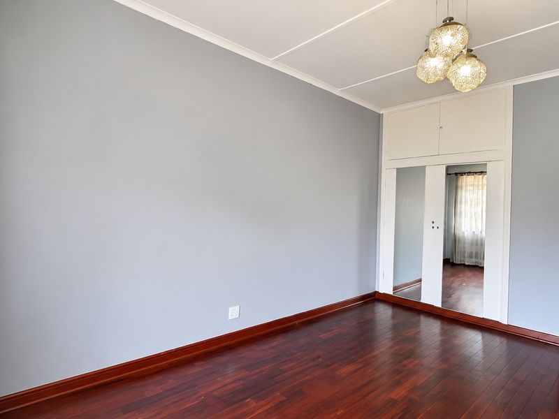 A bright, empty bedroom featuring polished hardwood flooring, built-in mirrored wardrobes with overhead storage, and neutral wall finishes.