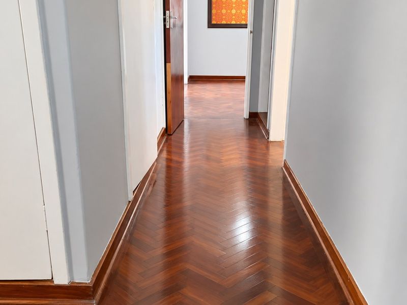 A bright, well-maintained hallway featuring polished herringbone parquet flooring and clean, neutral wall finishes leading to adjacent rooms.