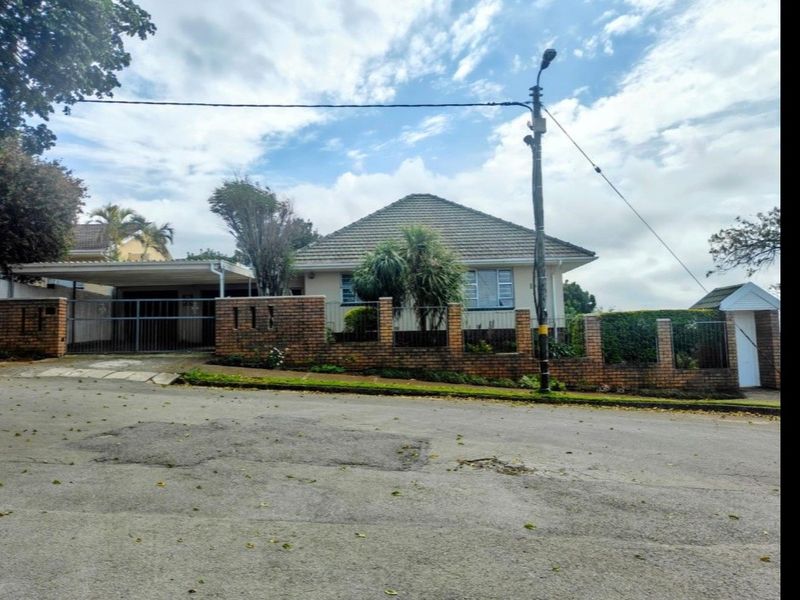 Front elevation of a single-story house featuring a tiled roof, brick boundary wall, and an attached carport with a metal gate.