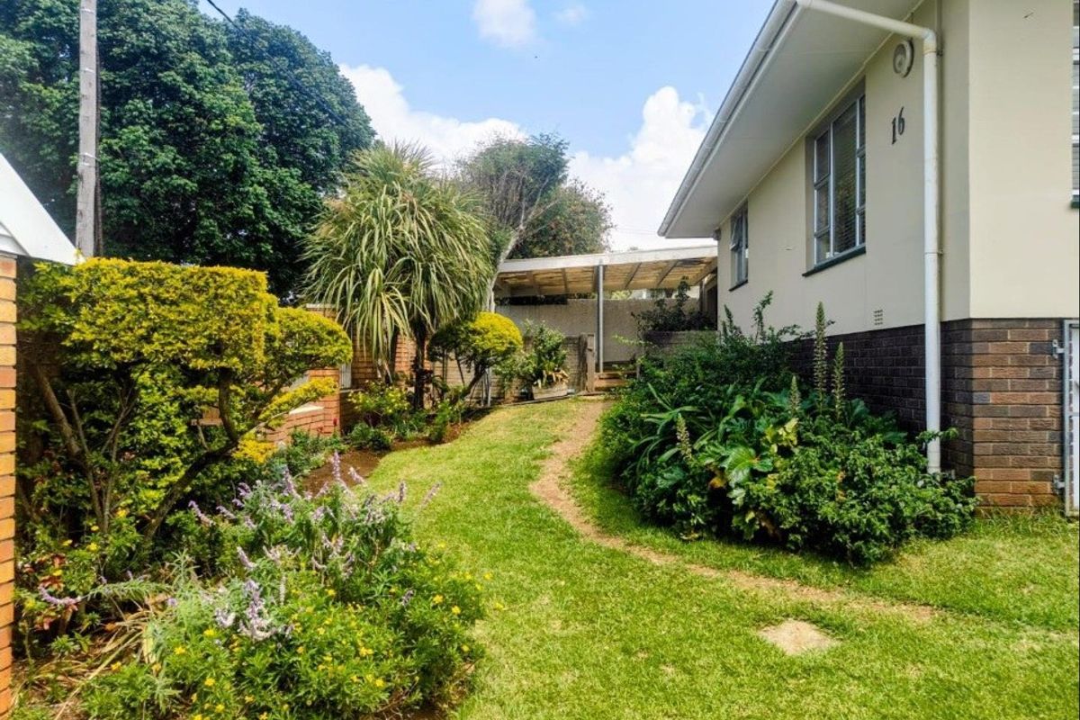 A view of the rear garden area featuring established landscaping, a lawn, and a covered outdoor patio structure attached to the side of the house.