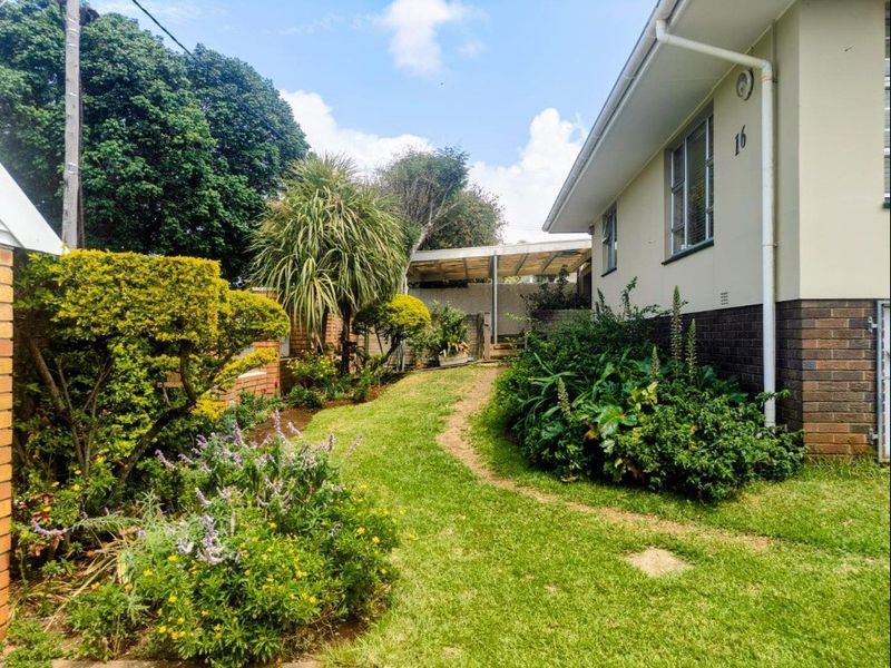 A view of the rear garden area featuring established landscaping, a lawn, and a covered outdoor patio structure attached to the side of the house.