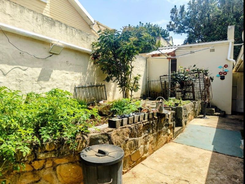 A rear courtyard area featuring a stone retaining wall, raised garden beds, and concrete paving, requiring some maintenance to the exterior wall and flooring.
