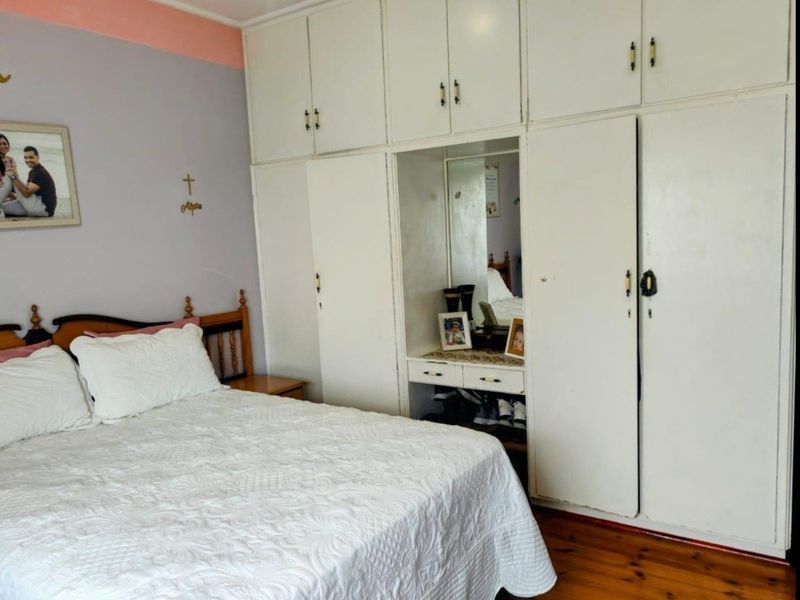 Bedroom featuring extensive built-in floor-to-ceiling cupboards with an integrated vanity area and warm hardwood flooring.