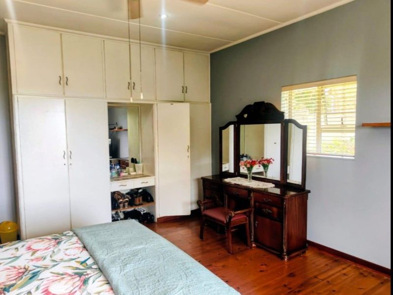 Spacious bedroom featuring warm wooden flooring, built-in floor-to-ceiling cupboards with a vanity nook, and a ceiling fan.