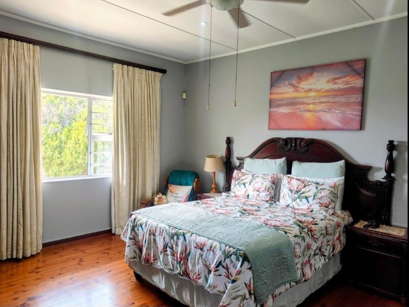 A well-lit bedroom featuring polished timber flooring, a ceiling fan, and a window with curtain treatments.