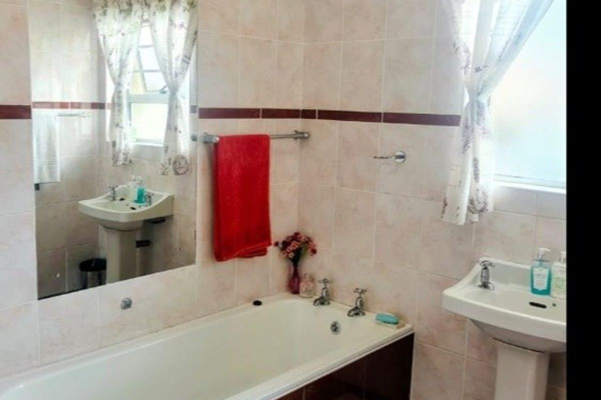 A functional bathroom featuring a pedestal washbasin, a built-in bathtub, and full-height wall tiling with a decorative border.
