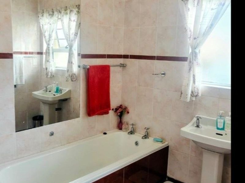 A functional bathroom featuring a pedestal washbasin, a built-in bathtub, and full-height wall tiling with a decorative border.