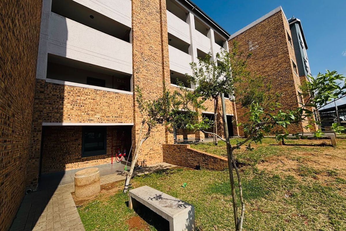 Exterior view of a multi-story apartment building featuring face brick construction, concrete balconies, and a landscaped garden area with a paved walkway.