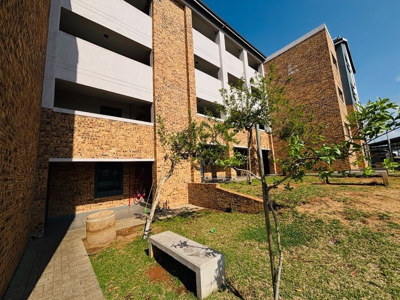 Exterior view of a multi-story apartment building featuring face brick construction, concrete balconies, and a landscaped garden area with a paved walkway.