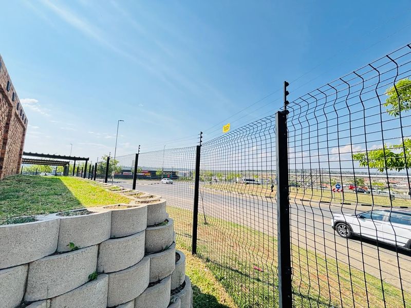Exterior view of the property boundary featuring a secure mesh fence with electric wiring and a tiered concrete retaining wall.