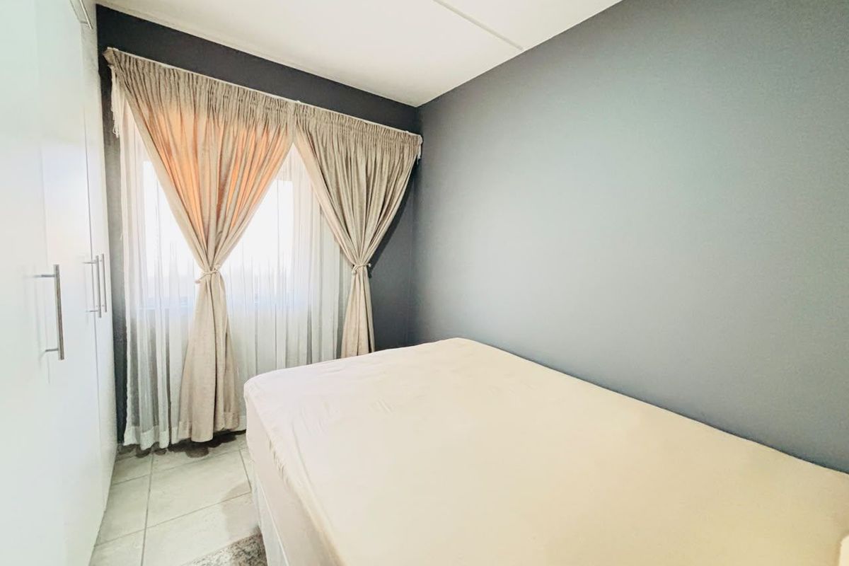 A compact bedroom featuring neutral grey walls, tiled flooring, and built-in cupboards providing ample storage space.