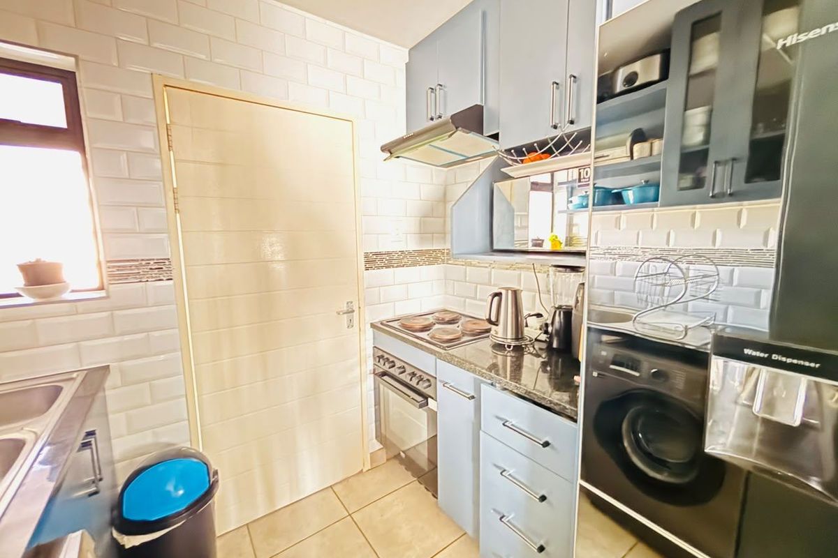 A functional kitchen featuring blue cabinetry, granite countertops, subway tile backsplash, and integrated appliances including a stove and washing machine.