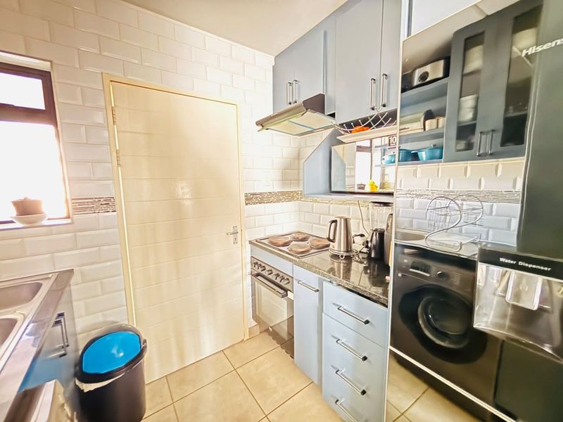 A functional kitchen featuring blue cabinetry, granite countertops, subway tile backsplash, and integrated appliances including a stove and washing machine.