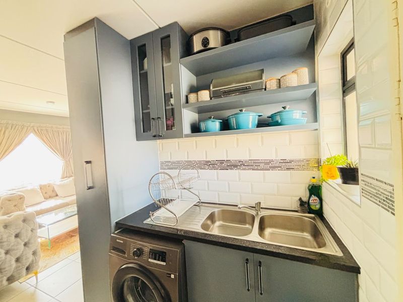 A compact, well-organized scullery featuring modern dark cabinetry, subway tile backsplash, double stainless steel sink, and an integrated washing machine.
