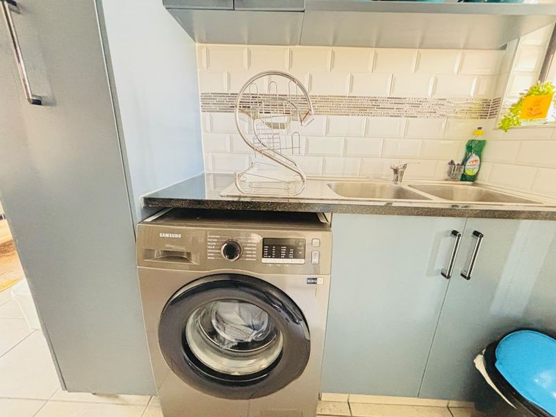 A functional laundry area featuring a stainless steel sink, granite countertop, subway tile backsplash, and built-in cabinetry with an integrated washing machine.