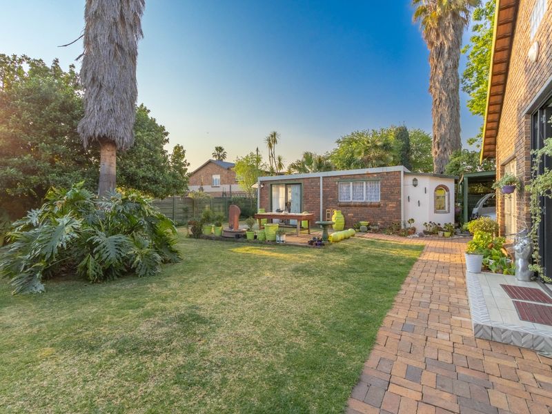 A well-maintained rear garden featuring a brick-paved walkway, a lush lawn, and a detached brick outbuilding with sliding glass doors.