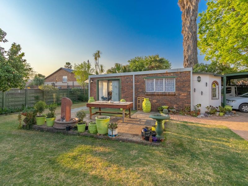 A rear view of the property featuring a brick facade, a paved patio area, and an attached carport, set within a landscaped garden.