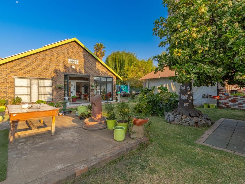 Rear view of the property featuring a brick facade, concrete patio area, and a spacious garden with mature landscaping.