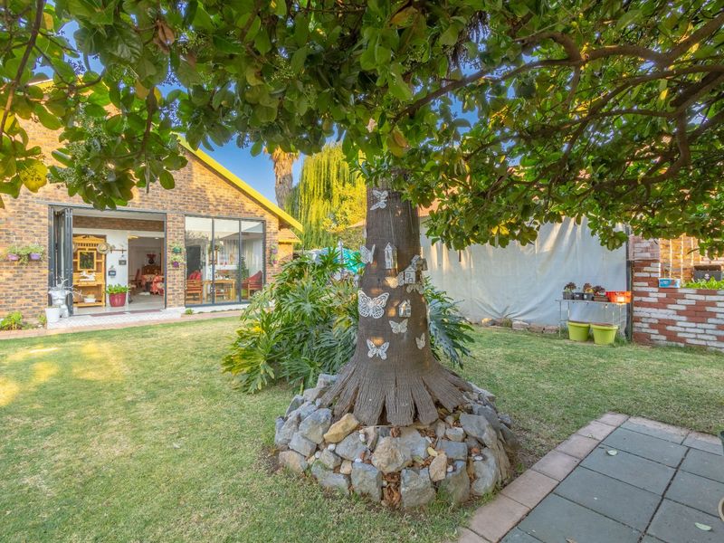 A view of the rear garden featuring a mature tree with stone base, paved patio area, and bi-fold doors leading into the home's living space.