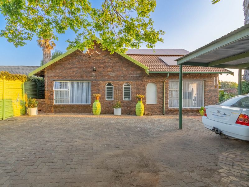 Front view of a face brick house featuring a paved driveway, carport, and solar panels installed on the tiled roof.