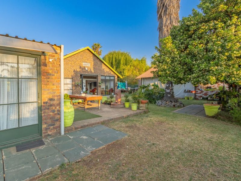 A spacious rear garden featuring a brick-faced dwelling, a paved patio area, and established trees, providing a private outdoor living space.