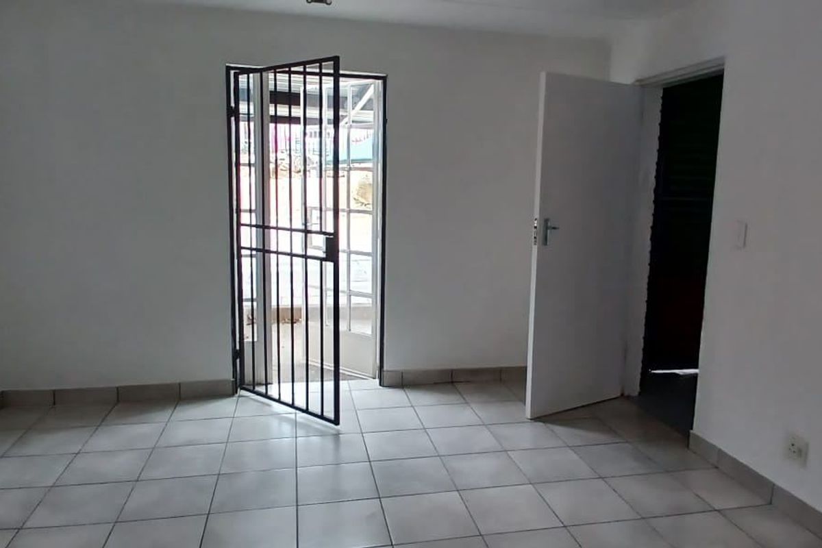 An empty, neutrally painted room featuring tiled flooring and a security gate leading to an exterior area.