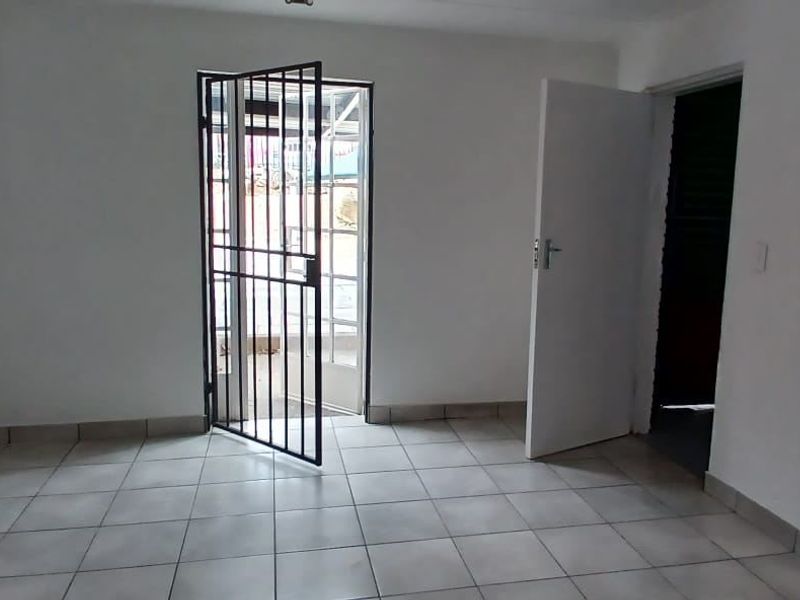 An empty, neutrally painted room featuring tiled flooring and a security gate leading to an exterior area.