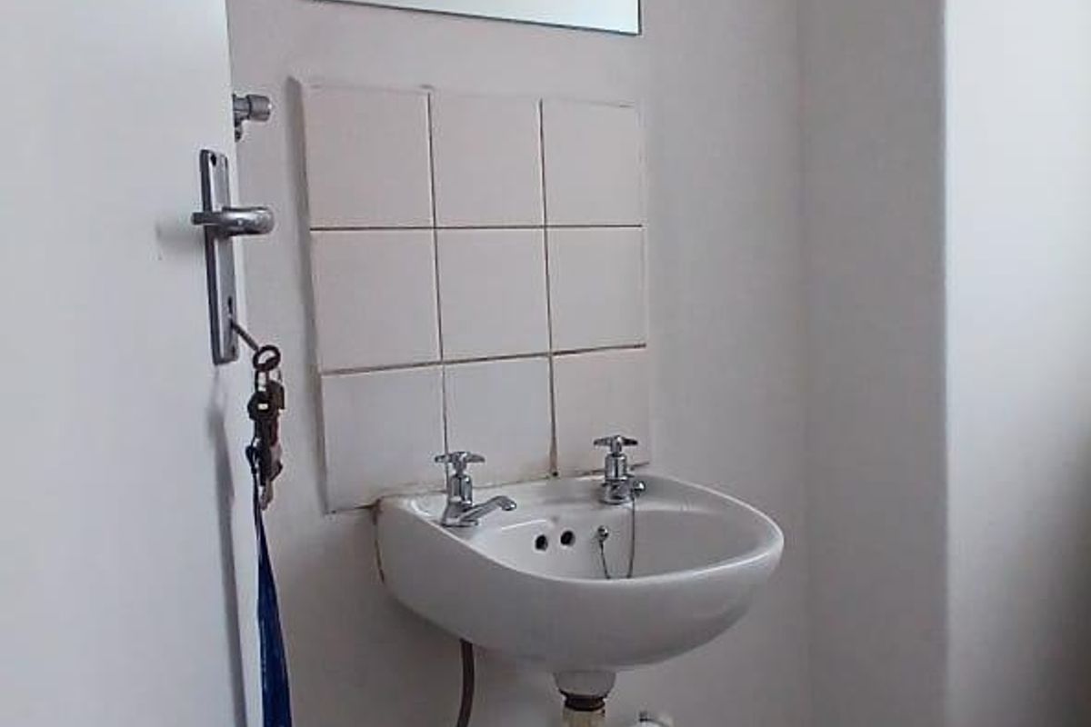 A functional bathroom space featuring a wall-mounted basin with tiled splashback, wall mirror, and ceramic floor tiling.