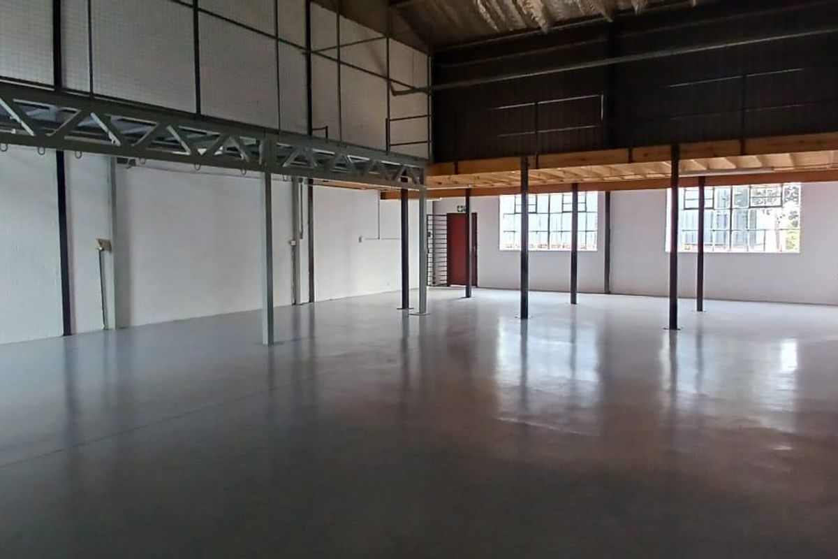 Spacious industrial utility area featuring polished concrete floors, a mezzanine level with steel support structures, and large windows providing ample natural light.