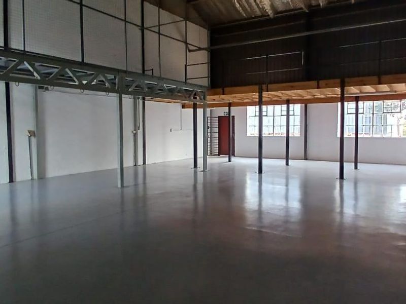 Spacious industrial utility area featuring polished concrete floors, a mezzanine level with steel support structures, and large windows providing ample natural light.