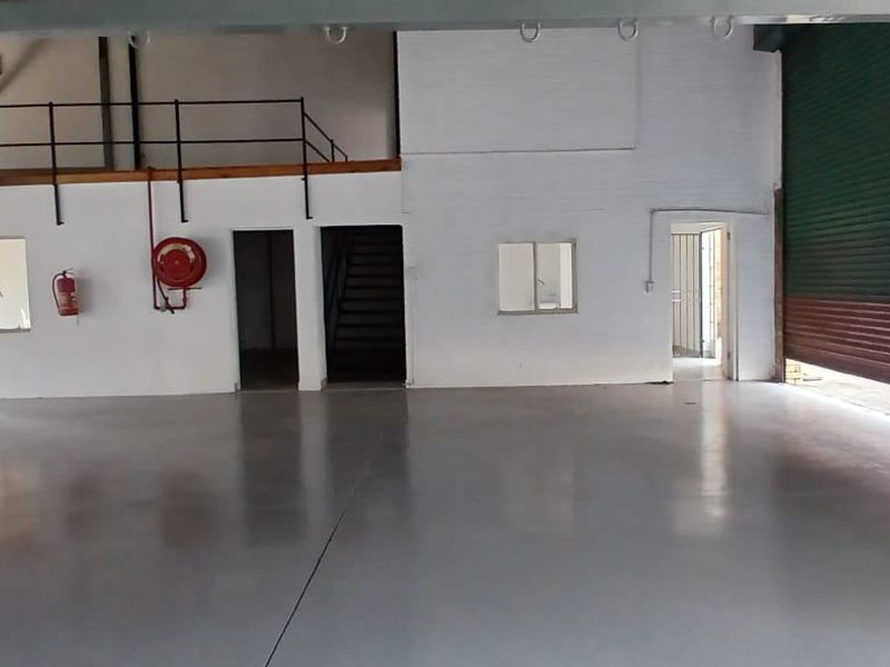 Spacious industrial warehouse unit featuring high ceilings, polished epoxy flooring, a mezzanine level, and a large roller shutter door for easy access.
